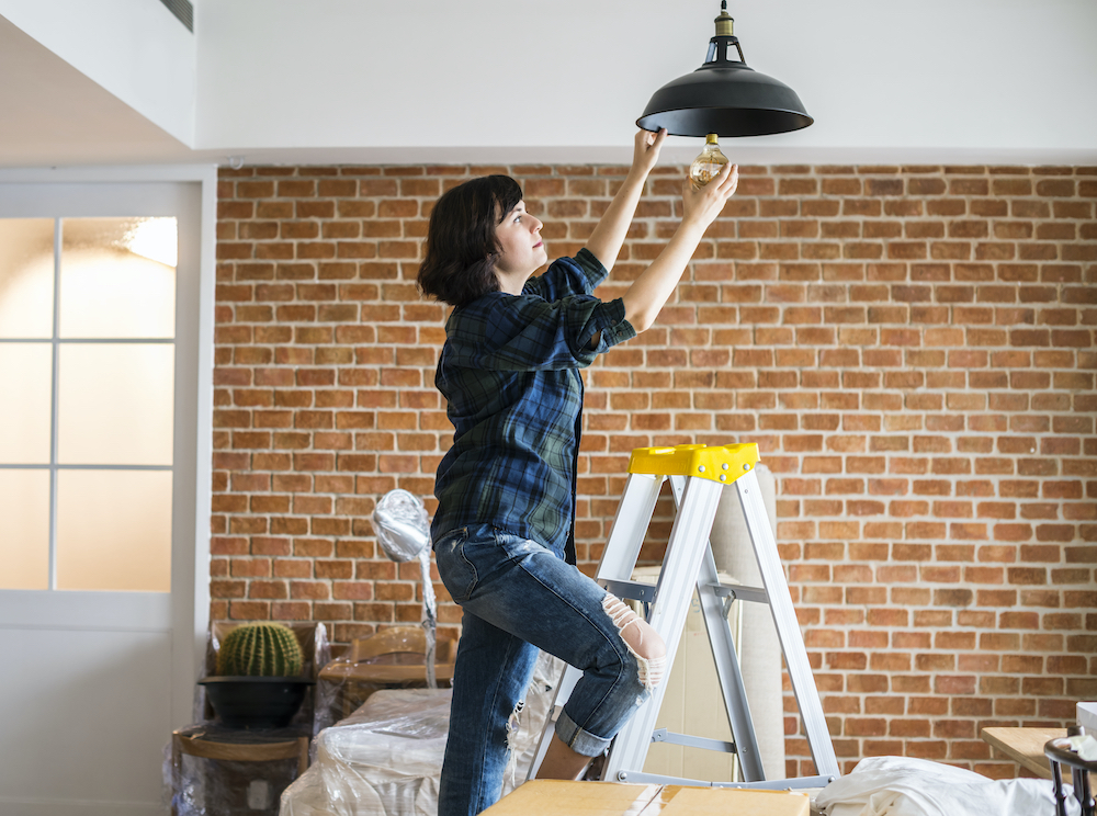 woman changing lightbulb while on a ladder ©Rawpixel
