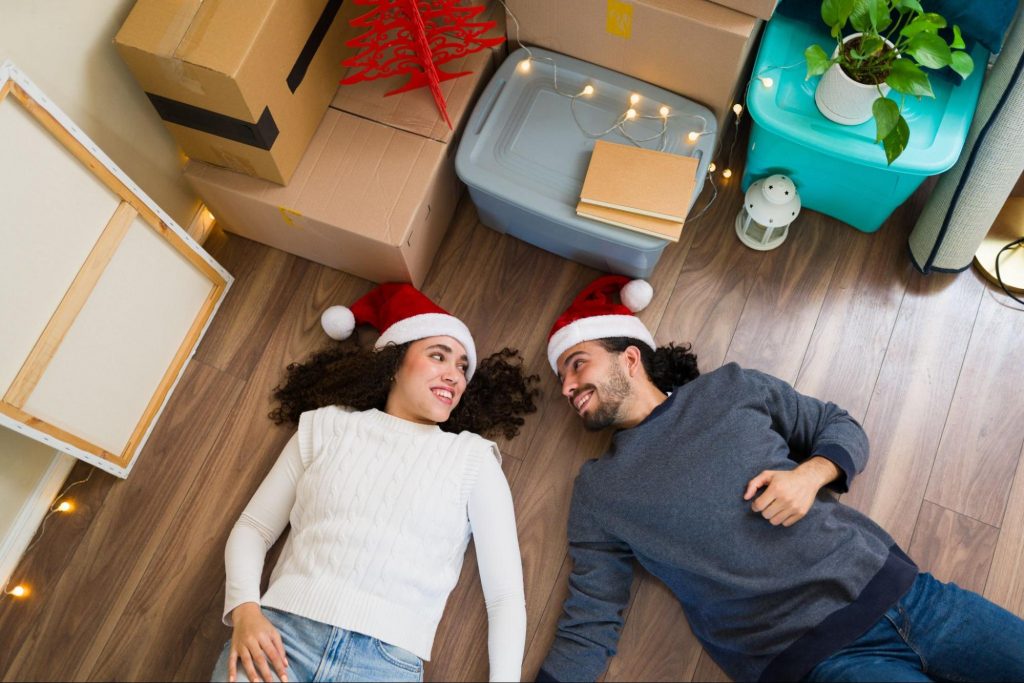A couple wearing Santa hats lying on the floor surrounded by moving boxes.
©antoniodiaz