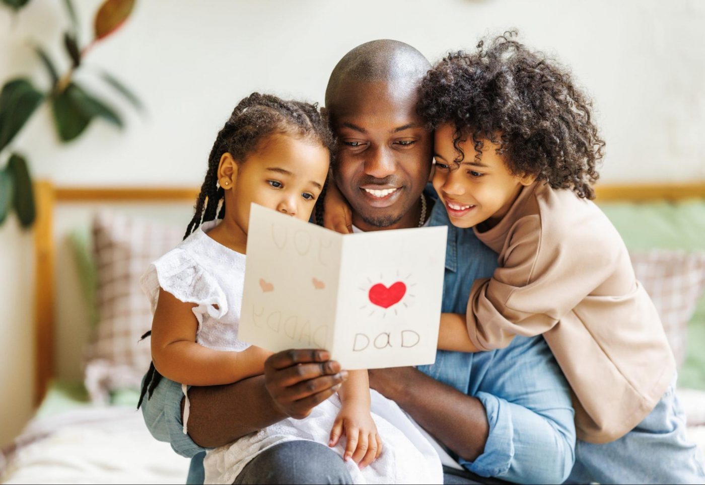 A father smiling while reading a handmade Father’s Day card with his two young daughters. ©Evgeny Atamanenko
