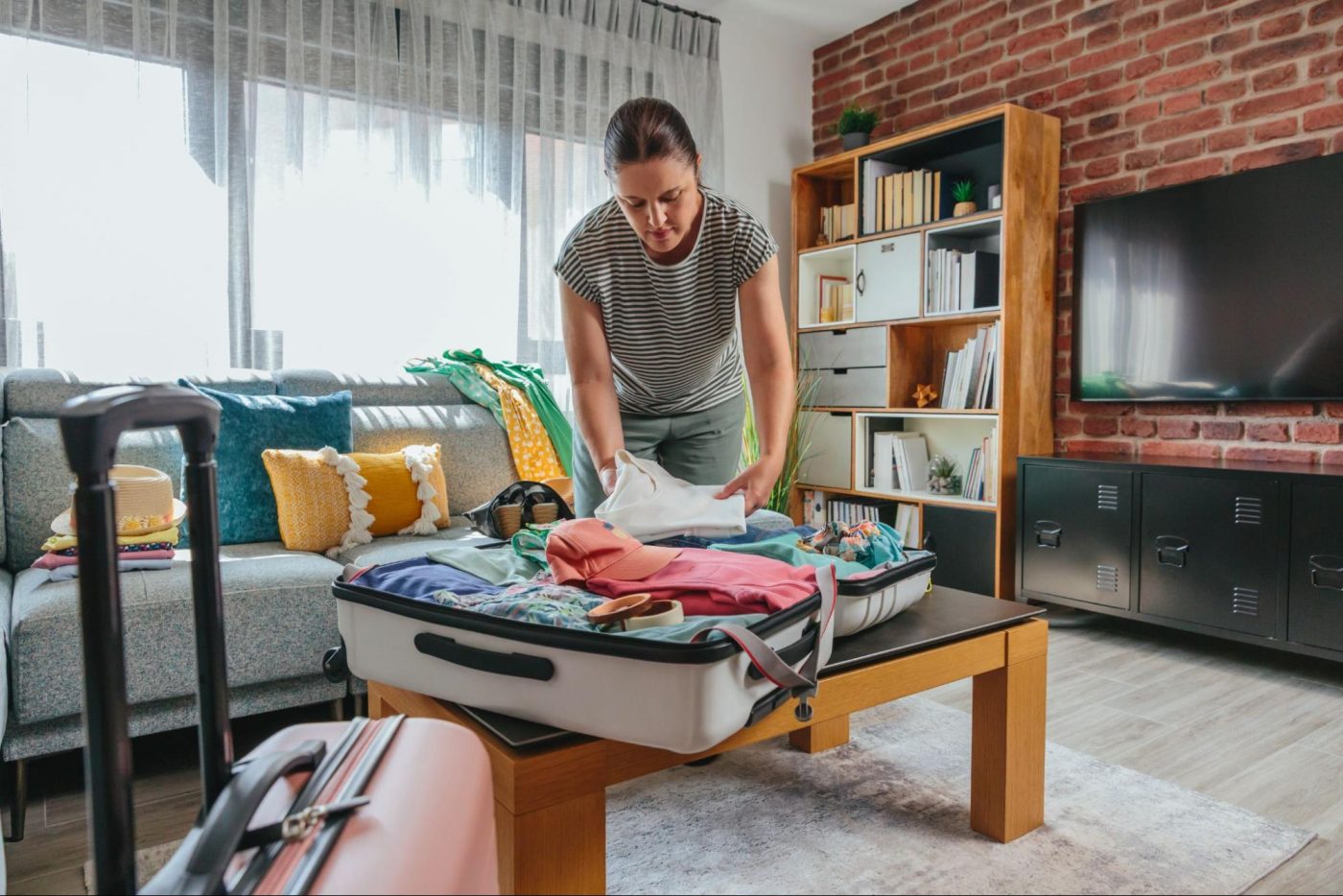 Woman packing clothes into a suitcase in a living room for a summer move ©David Pereiras