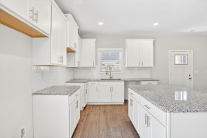 Open-concept white kitchen with granite countertops in a low-maintenance home by Peachtree Building Group.