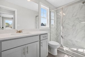 Modern bathroom in a new home at The Cottages at East Lanier in Fayetteville, GA, featuring a grey vanity and tiled walk-in shower. 
