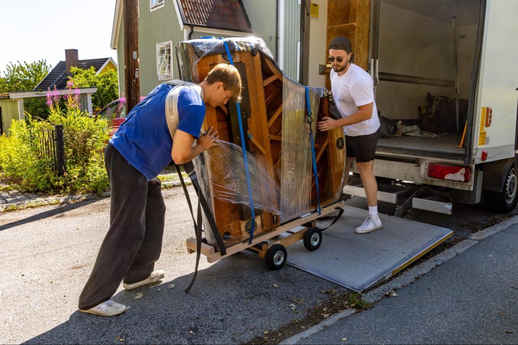 Two professional movers loading a wrapped piano onto a moving truck ramp
©Schager